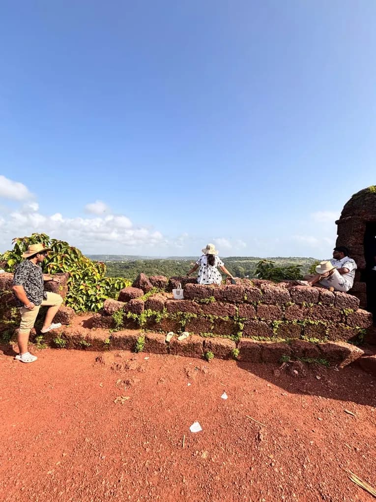 Colleagues in straw hats sitting and standing along the red laterite ramparts of the fort, green countryside beyond.