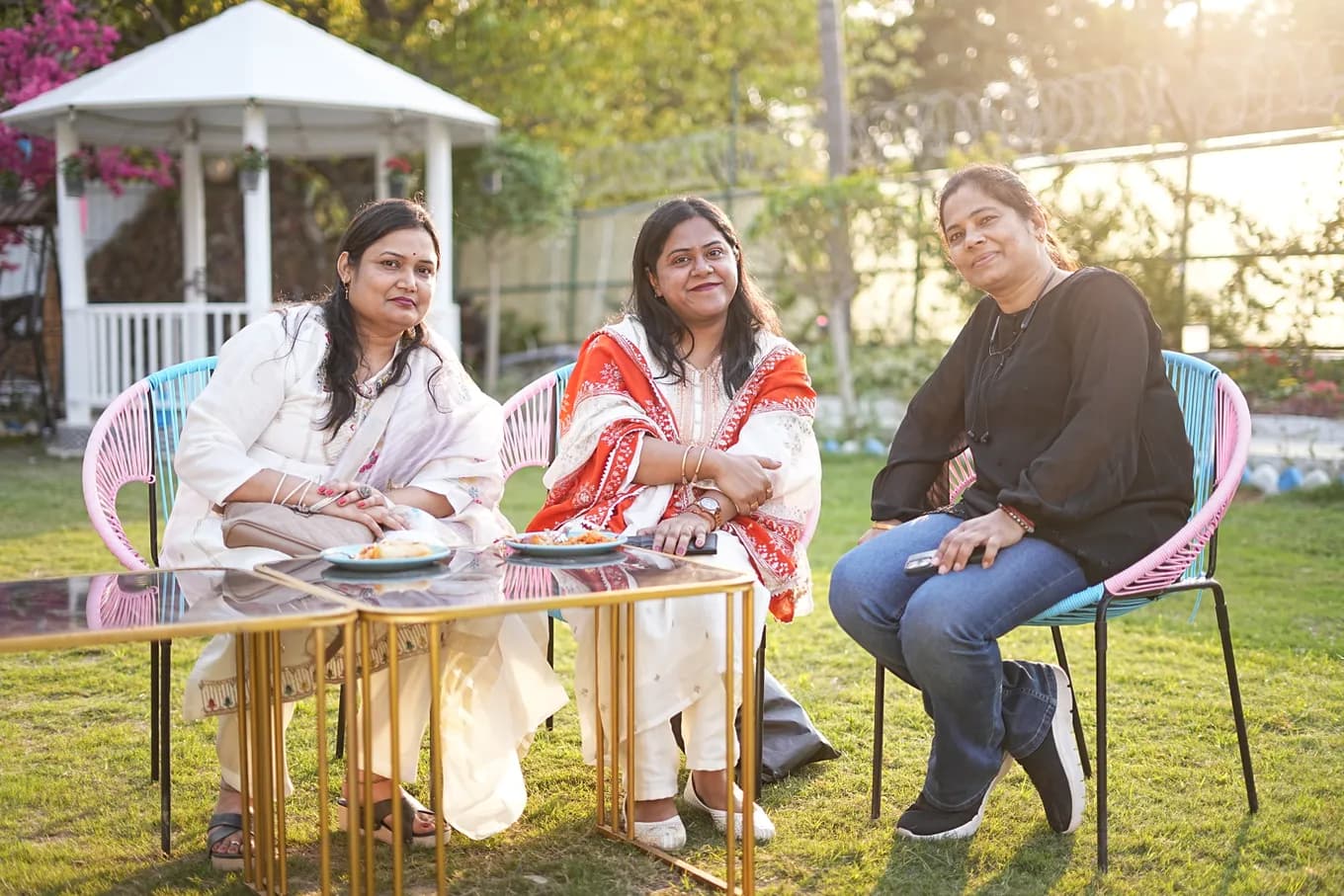 Three colleagues at a glass table on the lawn beside the white gazebo, the late afternoon sun behind them.