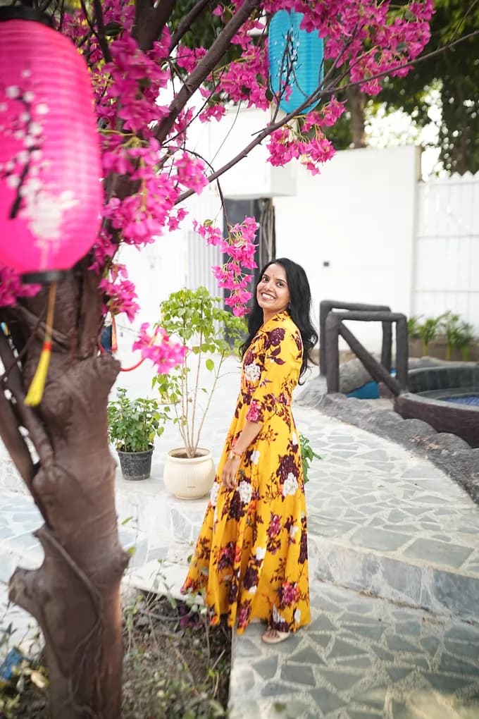 A colleague in a yellow floral dress standing under pink bougainvillea and a pink paper lantern at the farmhouse.