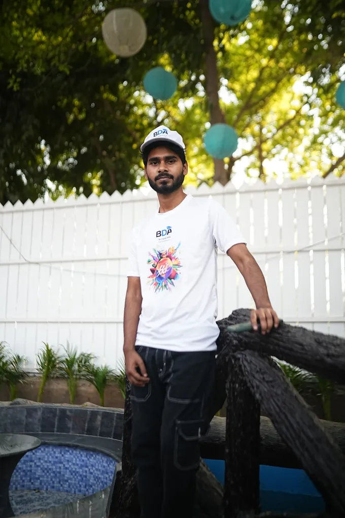 A colleague in a white cap and Holi t-shirt at the log railing in front of the white picket fence.