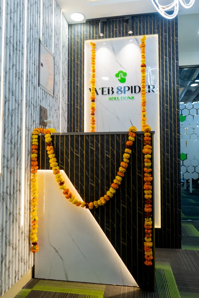 The marble reception desk of the new office with a marigold garland draped across its front, the Web Spider Solutions logo lit on the panel behind.