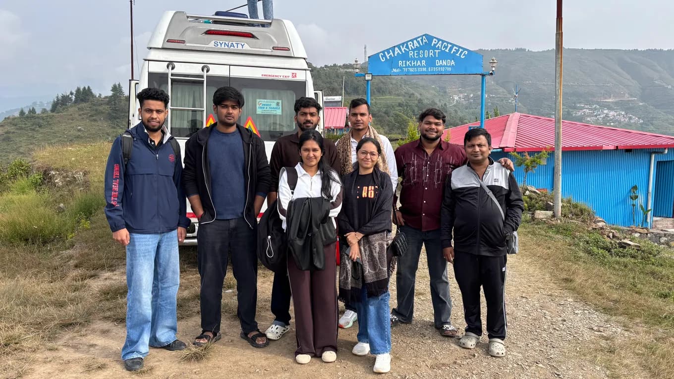 Eight team members in front of the white minibus under the Chakrata Pacific Resort sign at Rikhar Danda, misty hills behind.