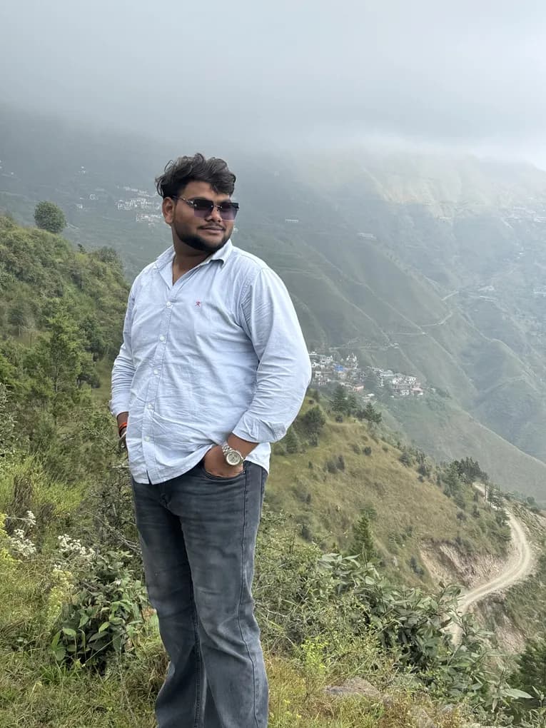 A colleague in sunglasses and a pale blue shirt standing on a ridge, a mountain road winding through the valley behind.
